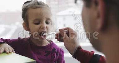 一个年轻的父亲在咖啡馆里用勺子喂小孩。